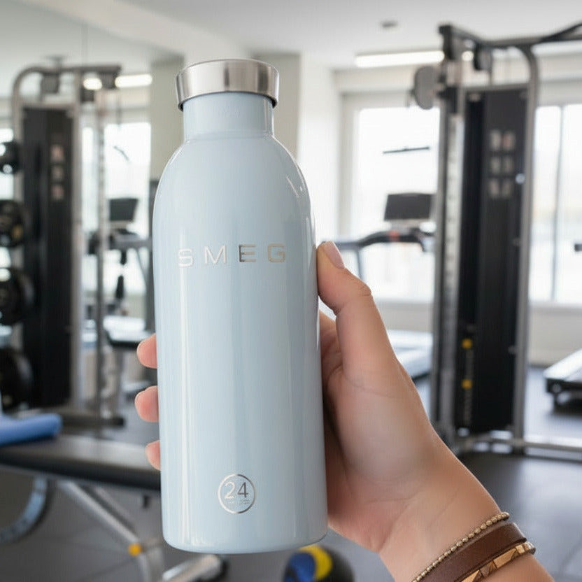 Hand holding a light blue water bottle with a brand logo in a gym setting