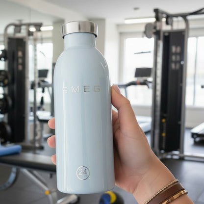 Hand holding a light blue water bottle with a brand logo in a gym setting