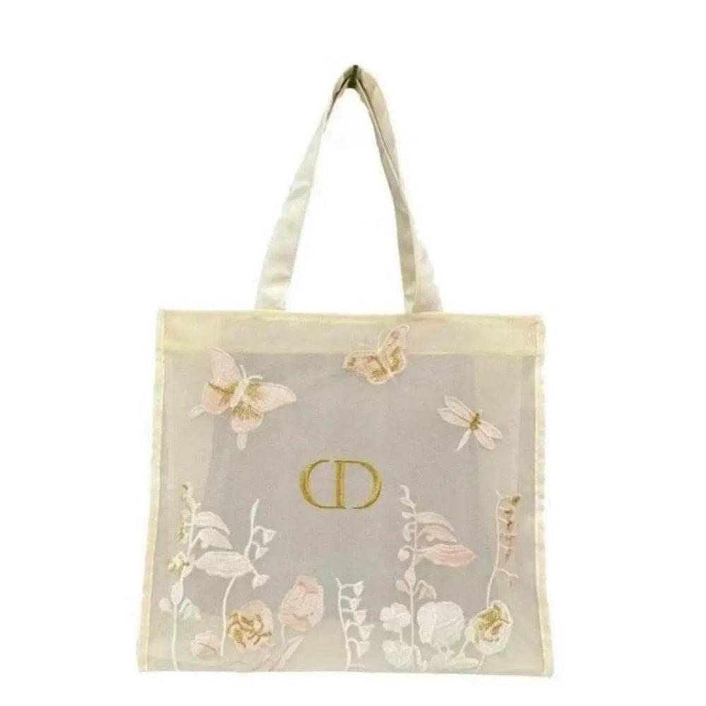 A sheer off-white mesh tote bag with a gold-tone CD logo in the center, decorated with embroidered butterflies, dragonflies, and floral motifs in soft pink, beige, and white. The bag features two wide shoulder straps and is photographed against a solid white background.