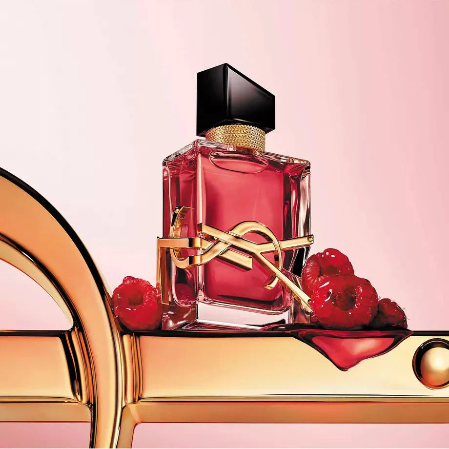 Saint Laurent fragrance bottle with a black cap and gold logo detail, filled with pink liquid, displayed on a gold surface with red berries against a soft pink background.