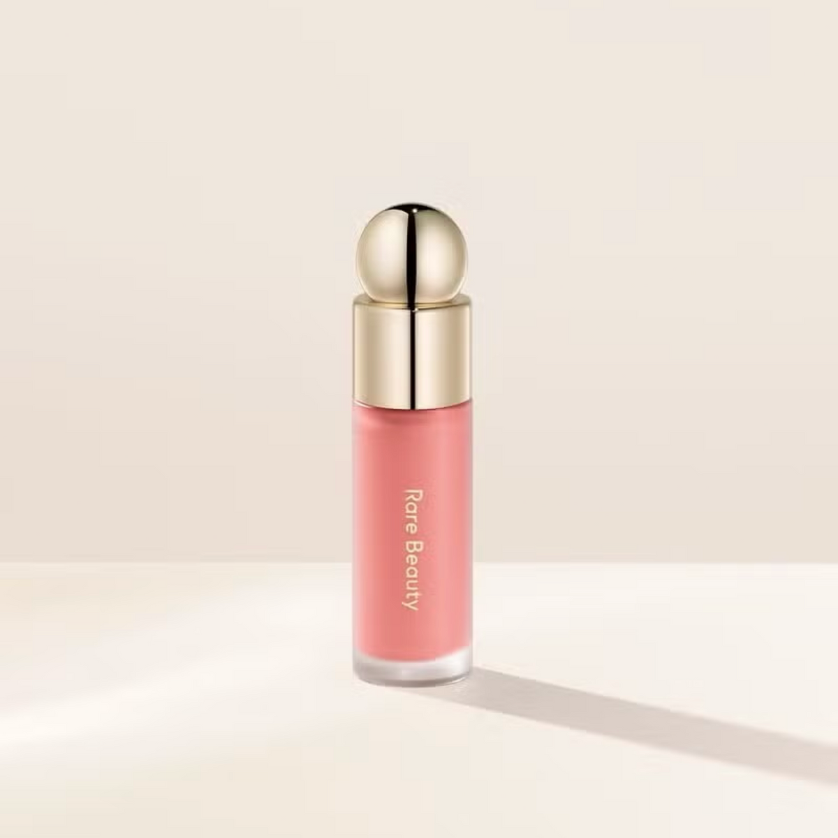 Pink lip gloss with gold cap on a beige background