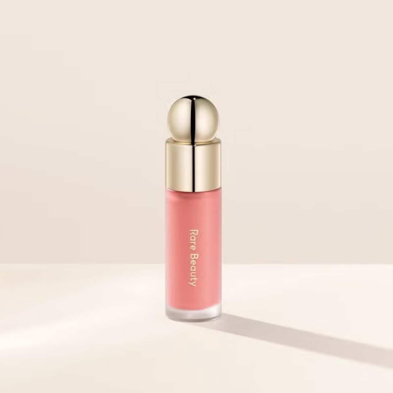 Pink lip gloss with gold cap on a beige background